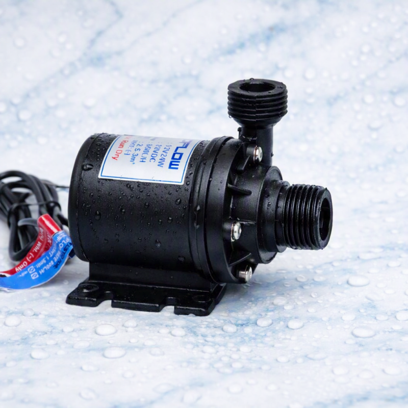 Compact black 12V DC water pump with cylindrical body, two threaded pipe connectors, and red/blue wires, placed on a wet surface with visible water droplets.